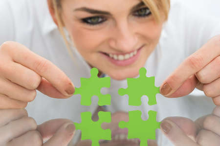 Portrait Of Happy Businesswoman Holding Pieces Of Jigsaw Puzzle On Desk