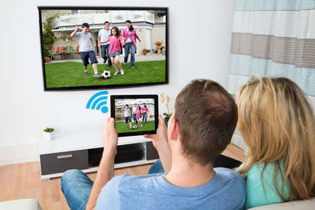 Couple Connecting Television And Digital Table Through Wifi Signal At Home