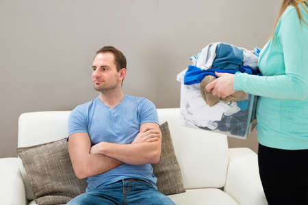 Woman Holding Laundry Basket While Man Sitting On Sofa