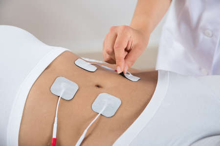 Close-up Of Therapist Placing Electrodes On Woman's Stomachの写真素材