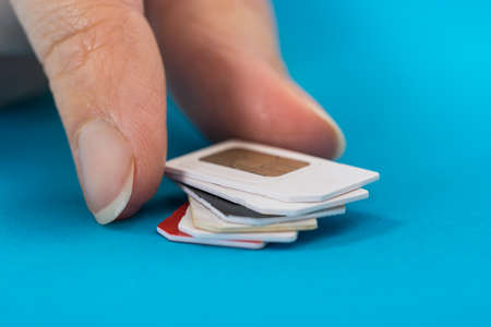 Close-up Of Hand Placing Stack Of Sim Card Over Blue Backgroundの写真素材