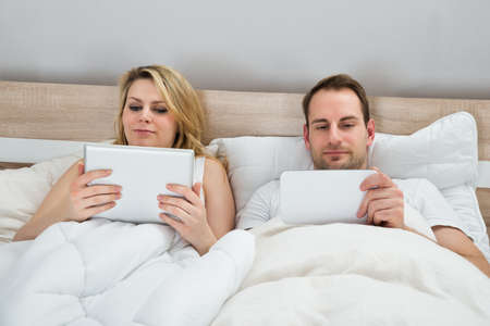 Couple With Digital Tablets In Bed At Homeの写真素材