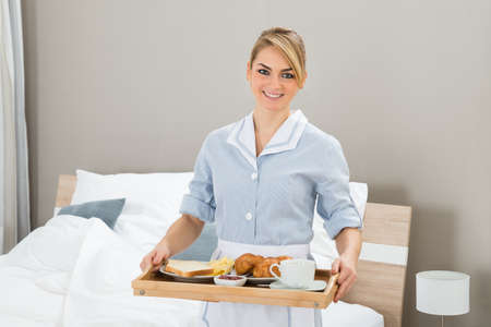 Happy Maid Carrying Breakfast Tray In Hotel Roomの写真素材