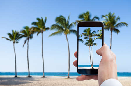 Close-up Of Person Hand Photographing Beach With Mobile Phoneの写真素材