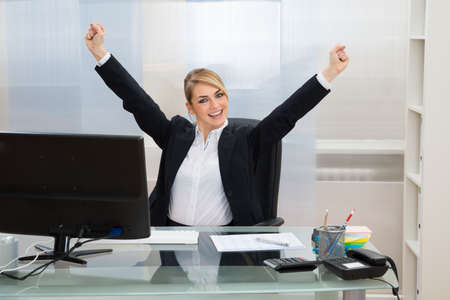 Young Happy Businesswoman Raising Hands In Officeの写真素材