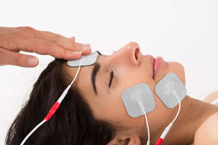 Close-up Of Hand Placing Electrodes On Young Woman's Faceの写真素材