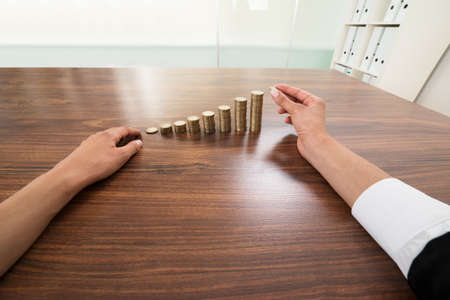Businessperson Hand Putting Coin To Stack Of Coins At Deskの写真素材