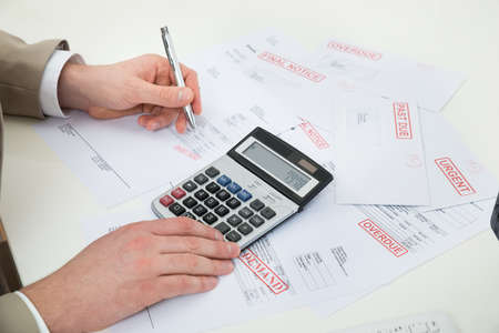 Close-up Of Businessperson Hand Calculating Bills At Desk