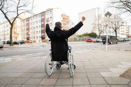 Rear View Of A Disabled Man On Wheelchair With Hand Raisedの写真素材