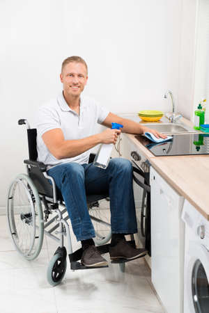 Young Happy Man On Wheelchair Cleaning Induction Stove In Kitchen Roomの写真素材