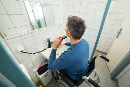 Disabled Man On Wheelchair Trimming Beard In Bathroomの写真素材
