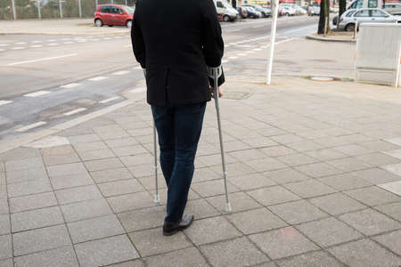 Rear View Of A Man Walking On Street Using Crutchesの写真素材