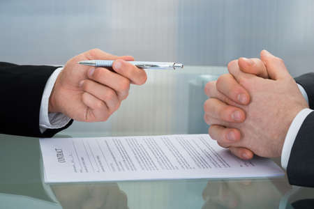 Close-up Of Businessman Giving The Pen To Sign A Contractの写真素材
