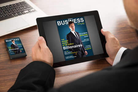 Close-up Of A Businessman Reading Online Magazine On Digital Tablet And Cellphone