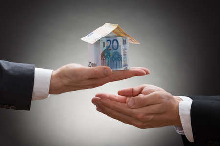 Close-up Of Businessman Hand Giving Money House In Hand Of Businesspersonの写真素材