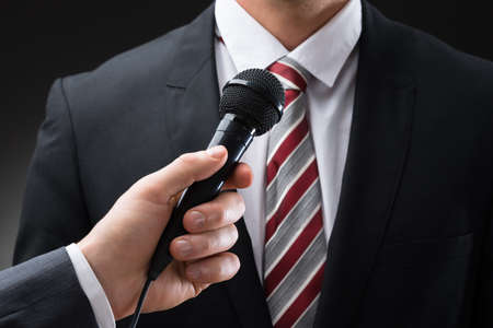Close-up Of A Person's Hand Holding Microphone In Front Of Businessmanの写真素材