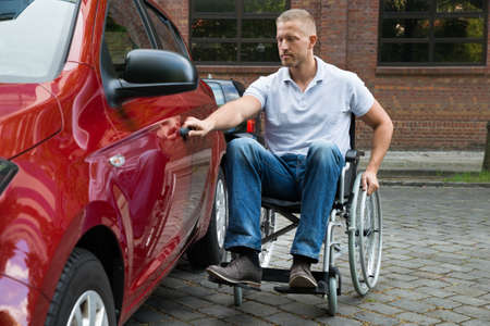 Portrait Of A Handicapped Man Sitting On Wheelchair Opening Door Of A Carの写真素材