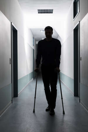 Silhouette Of Disabled Man Walking With Crutches In Hospitalの写真素材