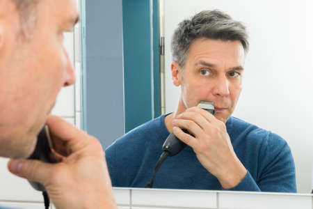 Portrait Of A Man Looking In Mirror Trimming Beard