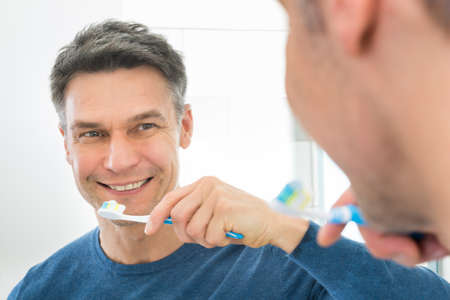 Close-up Of A Man Looking In Mirror Holding Toothbrushの写真素材