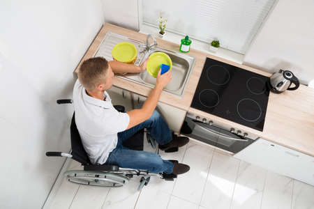 High Angle View Of Disabled Man On Wheelchair With Sponge Washing Dishesの写真素材