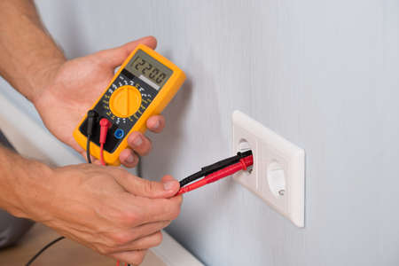Close-up Of Person Hand Metering Socket Voltage With Digital Multimeter