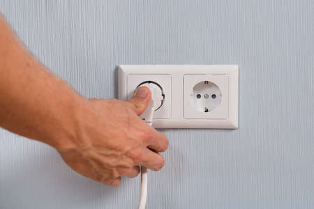 Closeup Of Hand Inserting An Electrical Plug Into A Wall Socketの写真素材