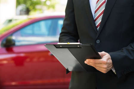 Close-up Of A Man Standing In Front Of Car Holding Clipboard In His Handの写真素材