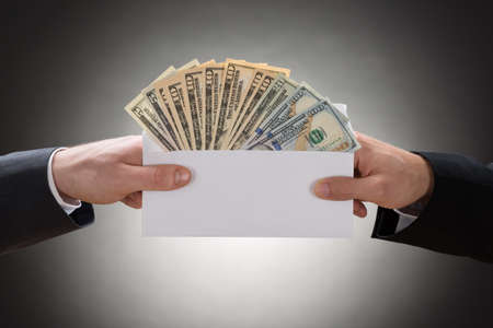 Close-up Of Two Businessman's Hand Holding Envelop Full Of Currency Note