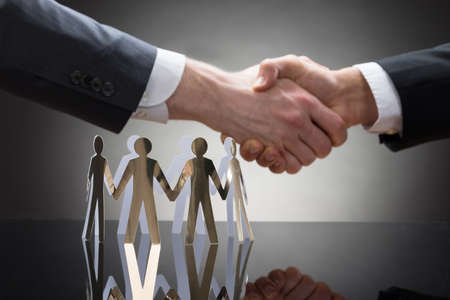 Close-up Of Businesspeople Shaking Hands With Paper Cutout Figuresの写真素材