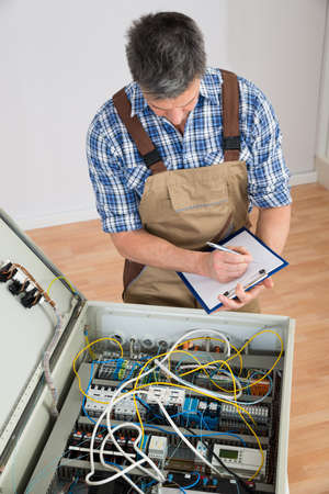 Electrician Looking At Fuse Box Holding Clipboard