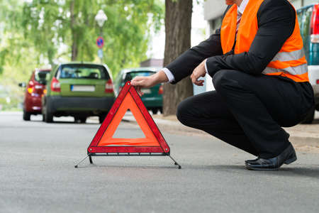 Close-up Of A Man Placing Warning Triangle With A Broken Down Cars