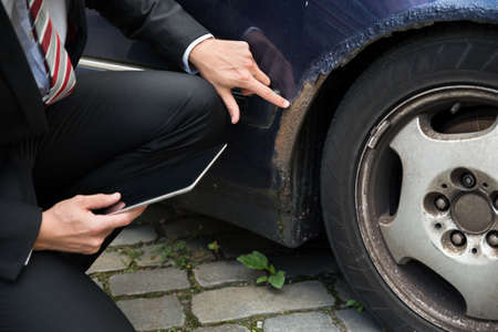 Insurance Agent Holding Digital Tablet Examining Car Damaged After Accidentの写真素材