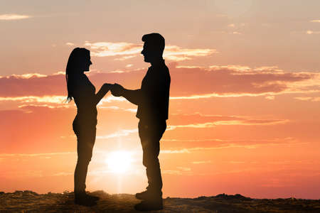 Silhouette Of Young Couple Against Dramatic Sky At Sunsetの写真素材