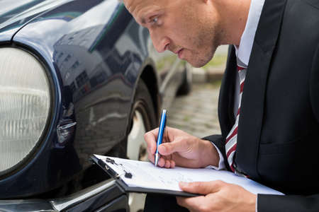 Close-up Of A Man Filling Insurance Form Near Damaged Carの写真素材