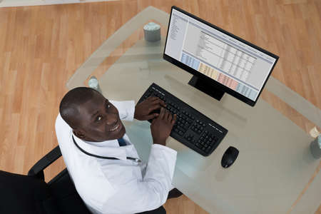 High Angle View Of Happy Young African Male Doctor Typing On Computer Keyboard