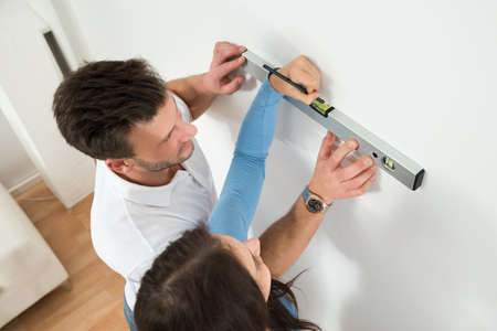 Happy Couple Marking With Pencil On Wall With Level In Houseの写真素材