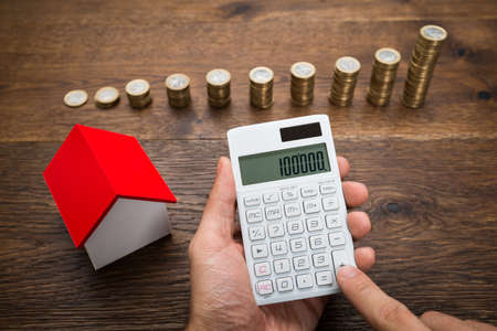 Businessman Using Calculator With House Model And Stack Of Coins On Deskの写真素材