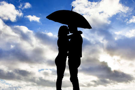 Silhouette Of Loving Couple Under Umbrella Against Cloudy Skyの写真素材