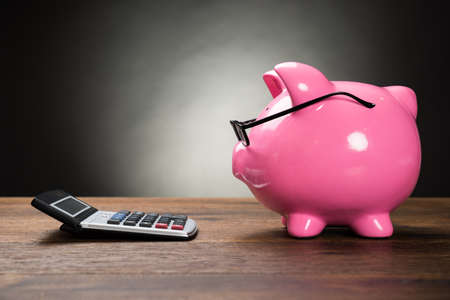 Piggybank With Eyeglasses And Calculator On Wooden Table