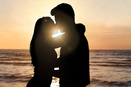 Silhouette Of Couple Kissing In Front Of Sea At Beach During Sunsetの写真素材