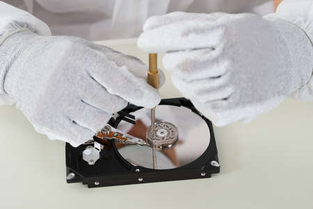 Close-up Of Person Hands Repairing Harddisk Using Screwdriver At Desk