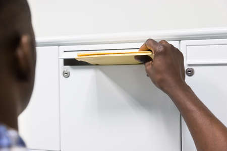 Close-up Of Person Hands Putting Envelope In Postbox