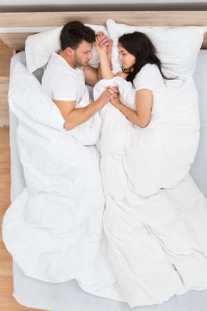 High Angle View Of Couple Holding Each Other's Hand Sleeping On Bed
