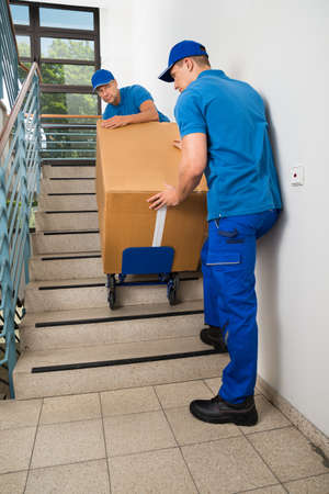 Two Male Movers Walking Downward With Box On Staircaseの写真素材
