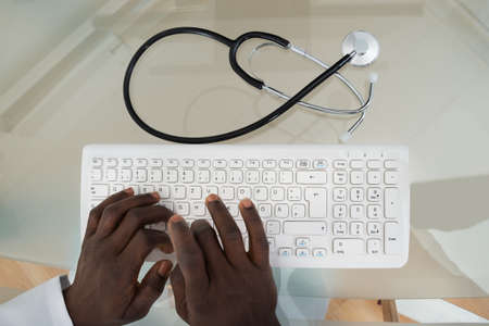 Close-up Of Male Doctor Hands Typing On Computer Keyboard At Deskの写真素材