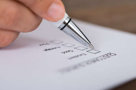 Close-up Of Person Hands Holding Pen Over Customer Survey Formの写真素材