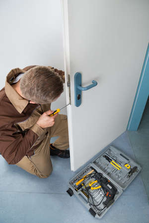 High Angle View Of Male Carpenter With Screwdriver Fixing Door Lock