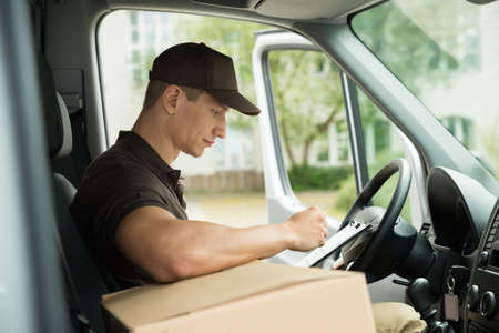 Young Delivery Man Checking List On Clipboard In Vanの写真素材