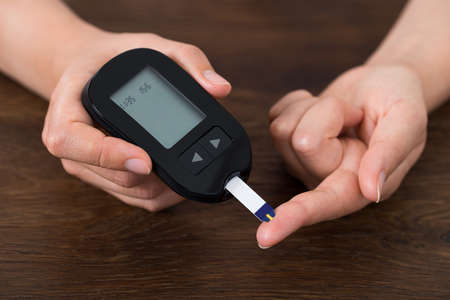 Close-up Of Person Hands Holding Glucometer At Deskの写真素材